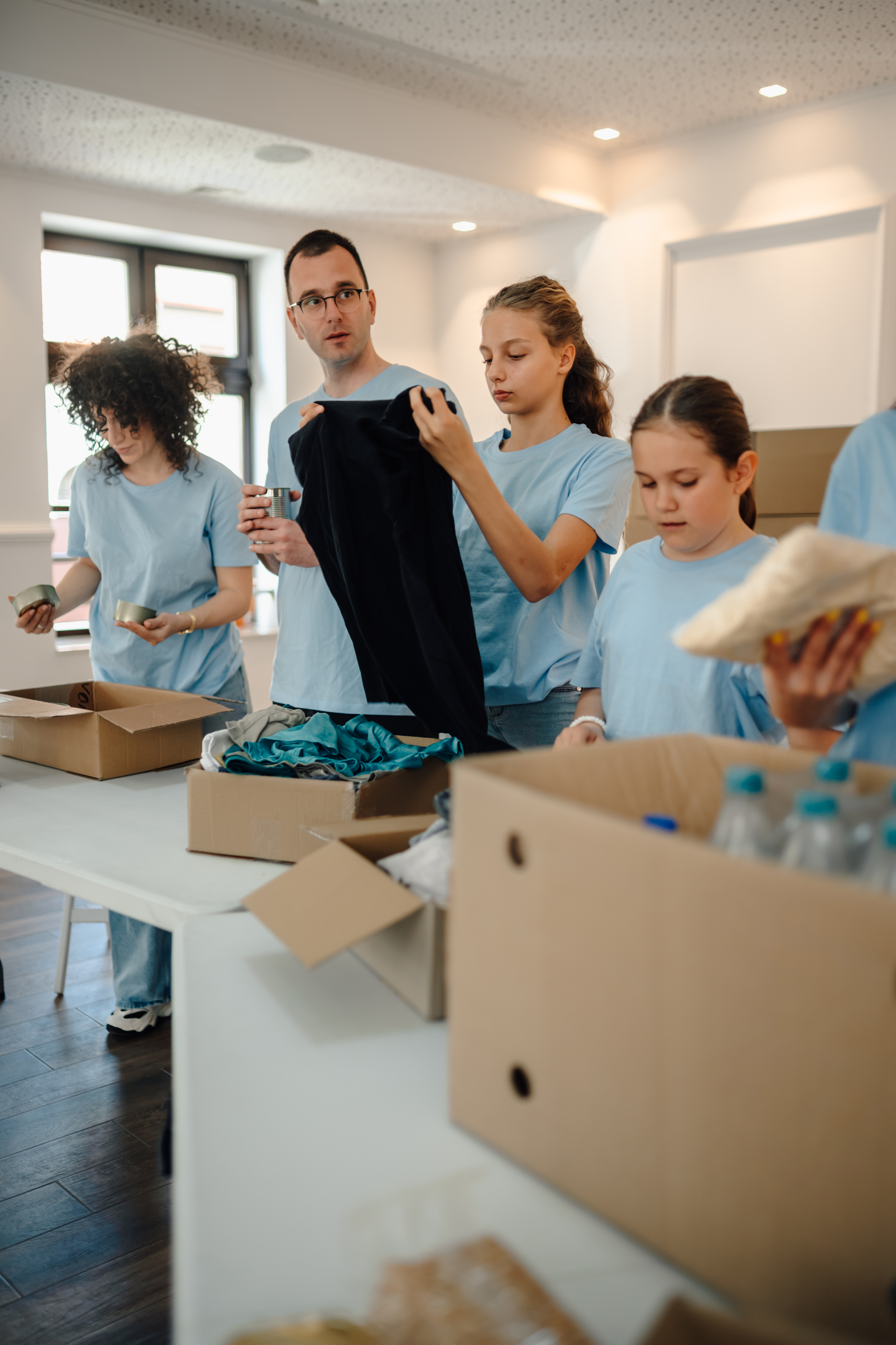 Group of volunteers working together, sorting donated items like clothing, canned goods and bottled water into cardboard boxes for charity